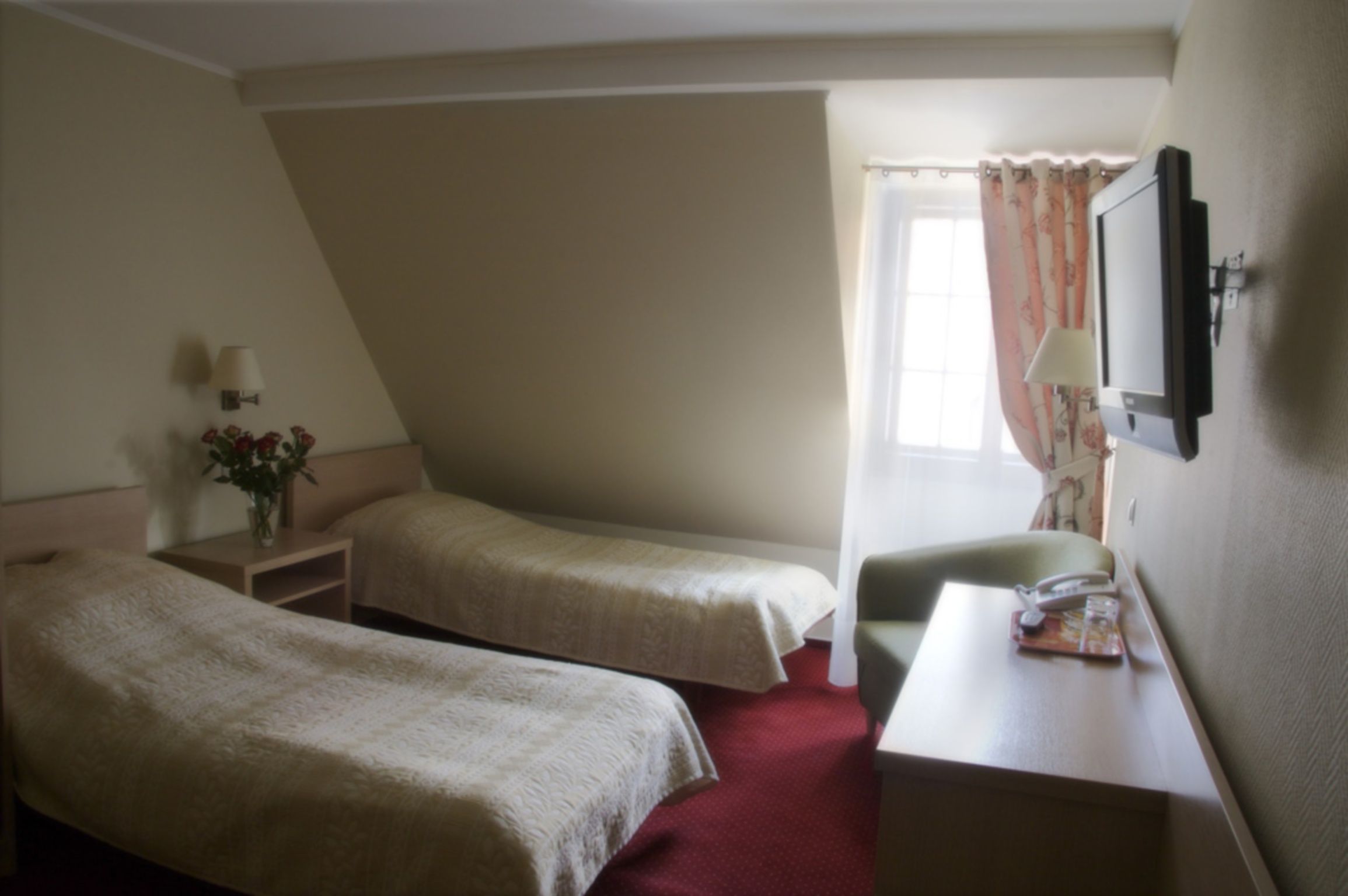 Habitación de hotel con dos camas individuales, un escritorio con teléfono, una lámpara y un televisor fijado a la pared.
