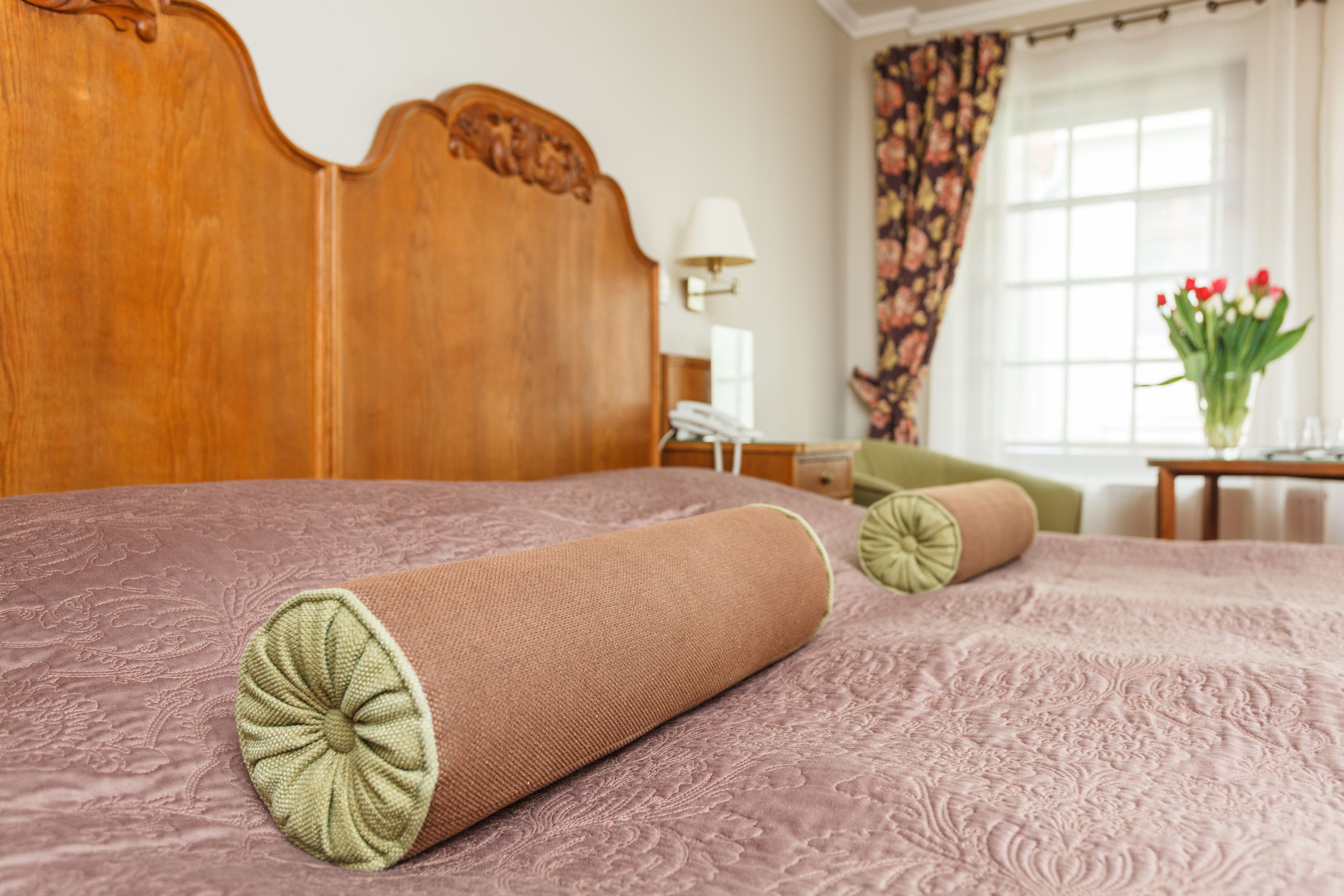 Ein ordentlich bezogenes Bett mit einer gemusterten Tagesdecke und zwei zusammengerollten Kissen.