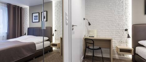 Habitación de hotel con cama, escritorio y silla. Se observa una pared de ladrillo blanco y una ventana con cortinas.