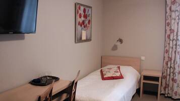 A hotel room with a bed, a desk with a chair, a television mounted on the wall, a small table, and a painting on the wall.
