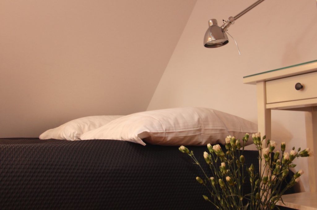 A bedroom with a bed, a bedside lamp, a nightstand, and a vase with flowers.