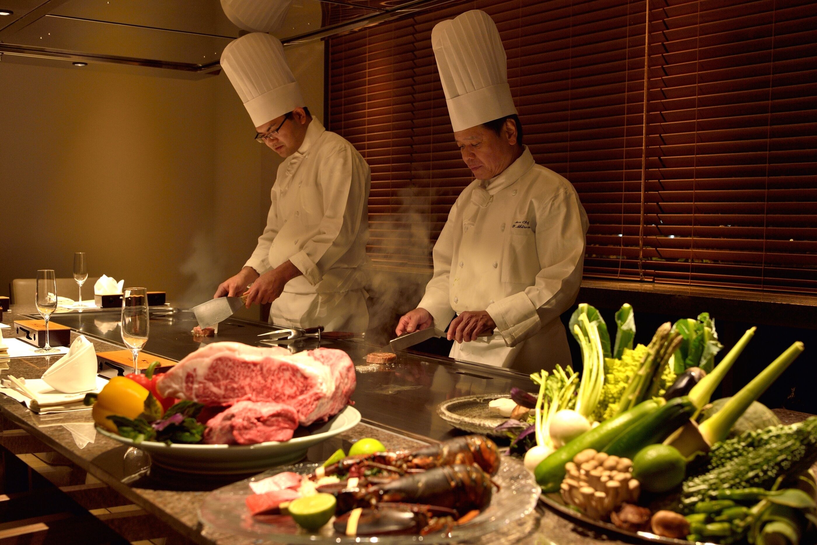 Dos chefs preparando comida en una parrilla, en un ambiente de restaurante.