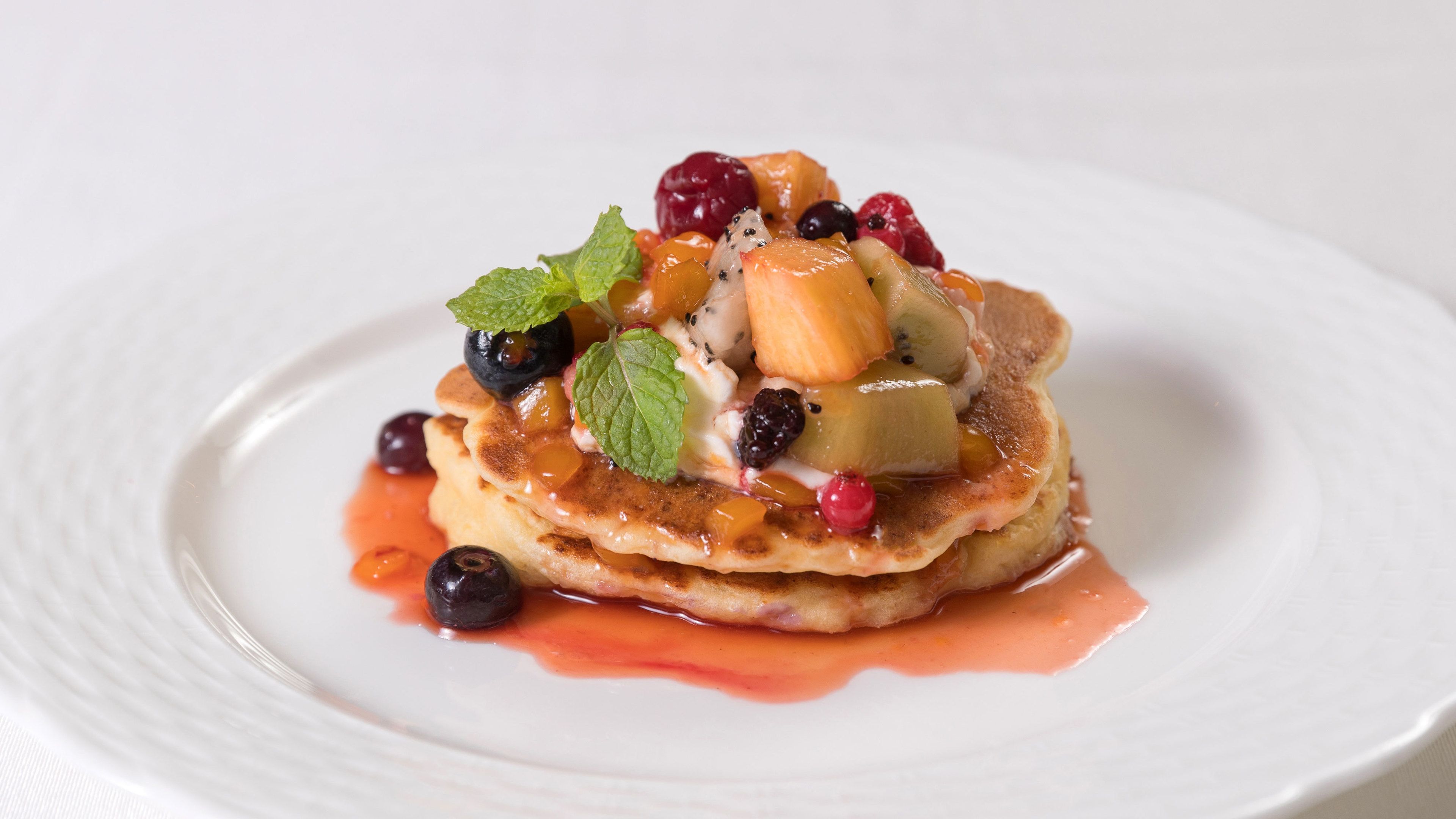 A stack of pancakes topped with fruit and syrup on a white plate.
