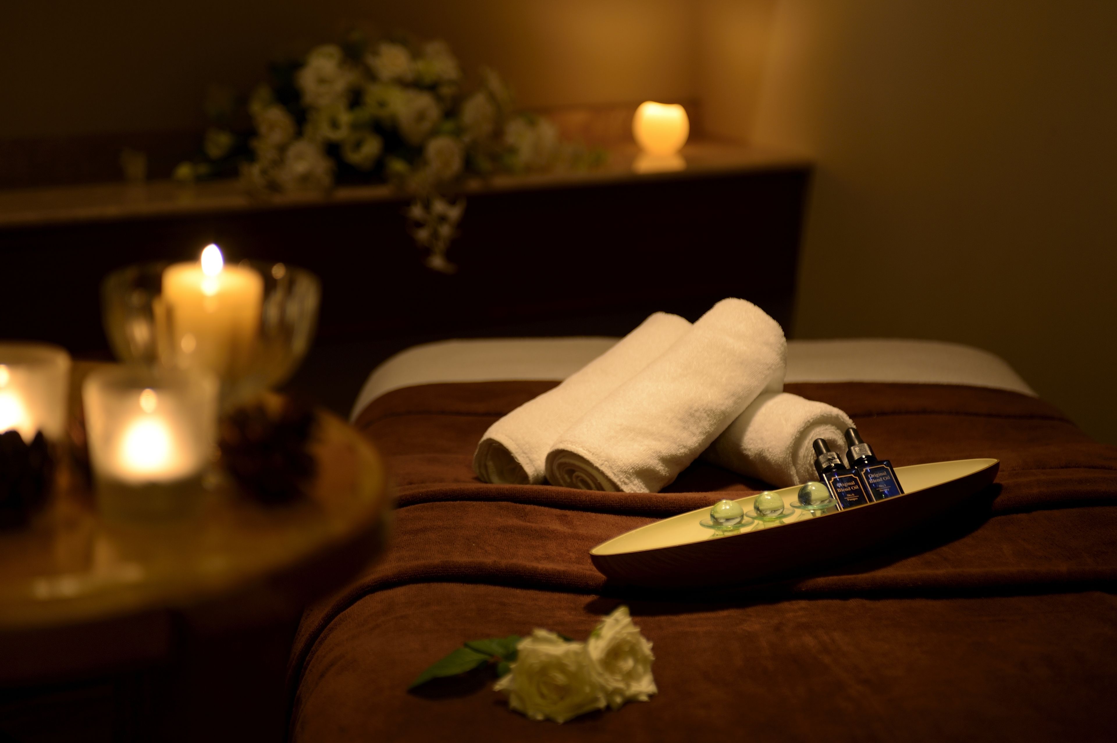 A spa setting with a bed, candles, a tray with toiletries, and a flower.