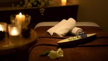 A spa setting with a bed, candles, a tray with toiletries, and a flower.