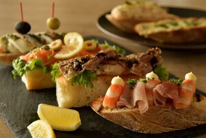 Variedad de aperitivos en una tabla de pizarra, incluyendo pan con ingredientes y adornos.