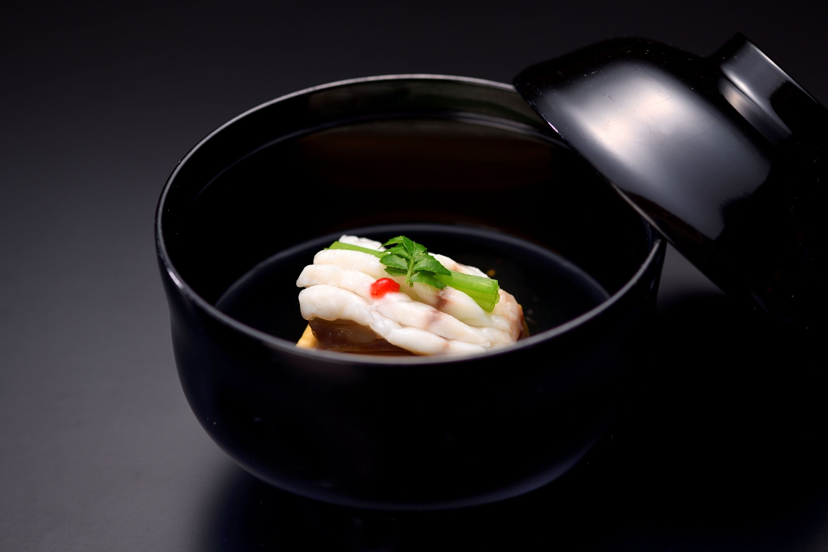 A black bowl with a white food item, garnished with green leaves and a red chili, on a dark surface.
