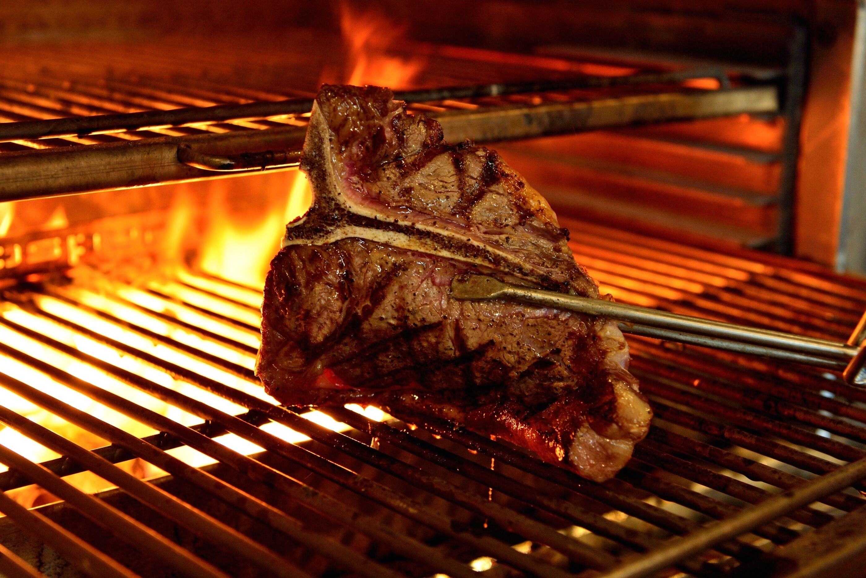 A steak being grilled on a grill with visible flames.