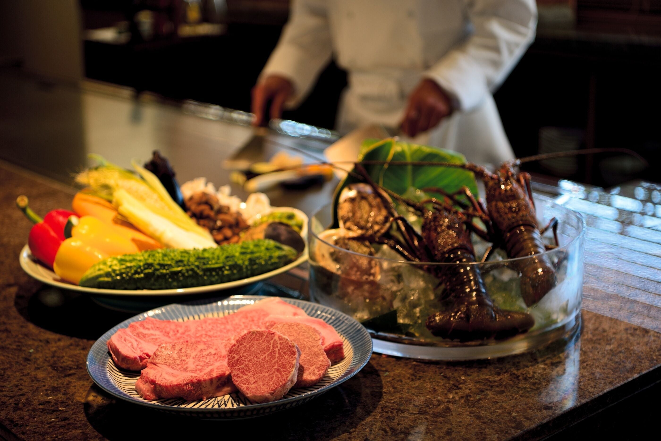 A kitchen counter with various food items including vegetables, a bowl of seafood, and a plate of meat.