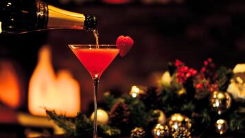 A cocktail being poured into a martini glass with a strawberry garnish, set against a blurred background with Christmas decorations.