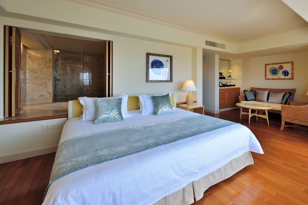 A hotel room with a large bed, a sitting area with a table and chairs, a shower area, and artwork on the walls.