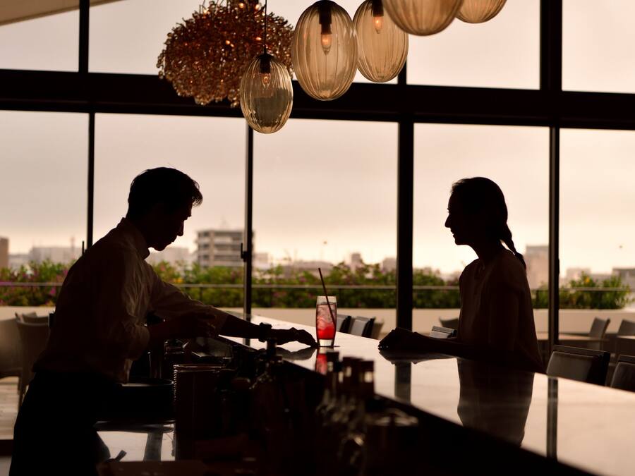 A bar area with a city view, large windows, and hanging light fixtures.