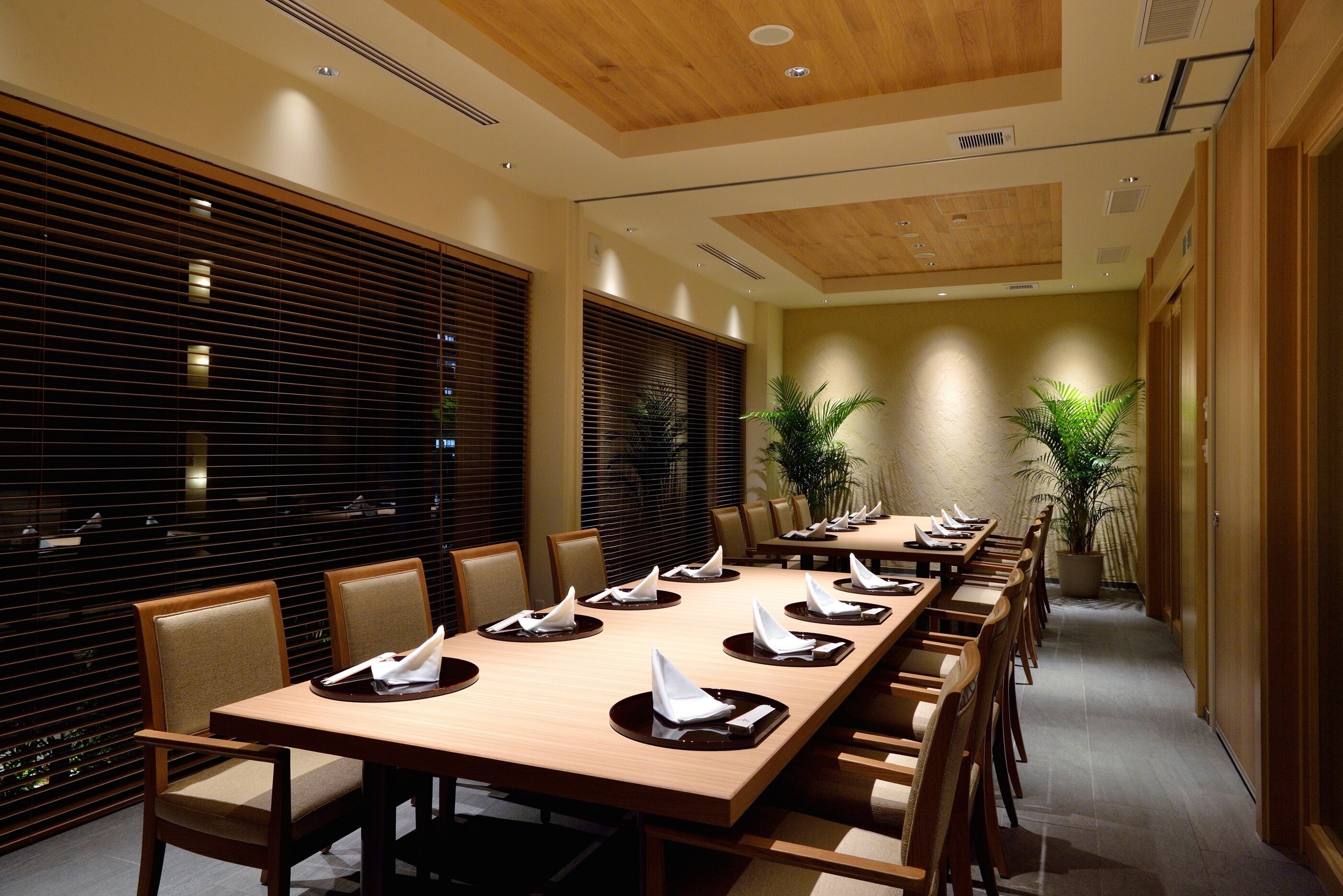 A conference room with long tables, chairs, and potted plants.