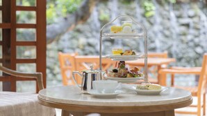 Un servicio de té de tres niveles sobre una mesa con una tetera y tazas, frente a una pared de piedra y sillas de madera.