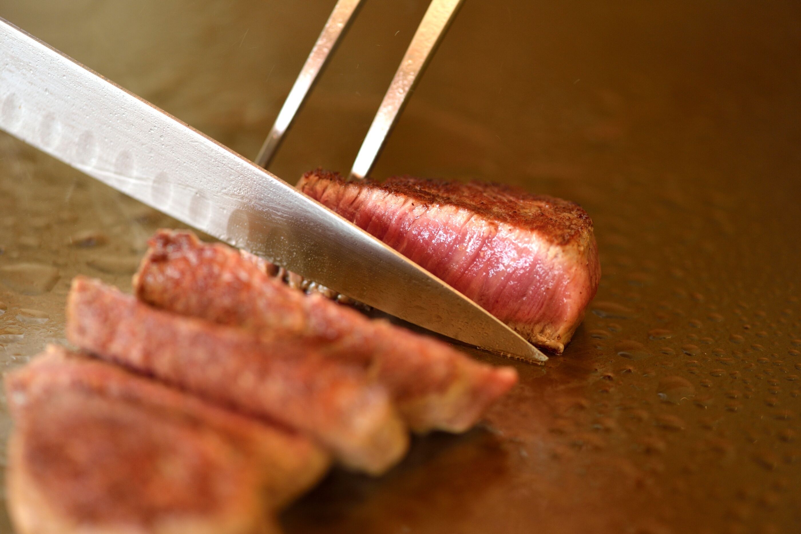 A knife cutting through a piece of meat on a cutting board.
