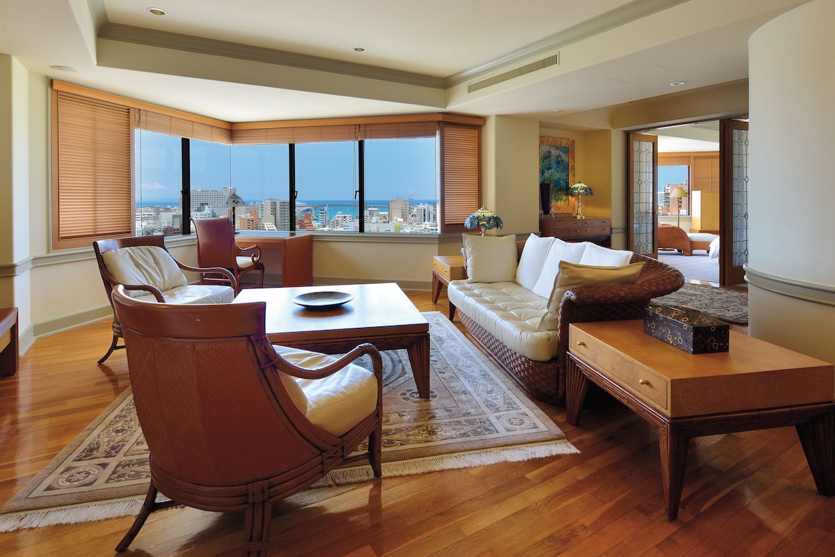 A spacious living room with a large window, a sofa, a dining table, and a chair.
