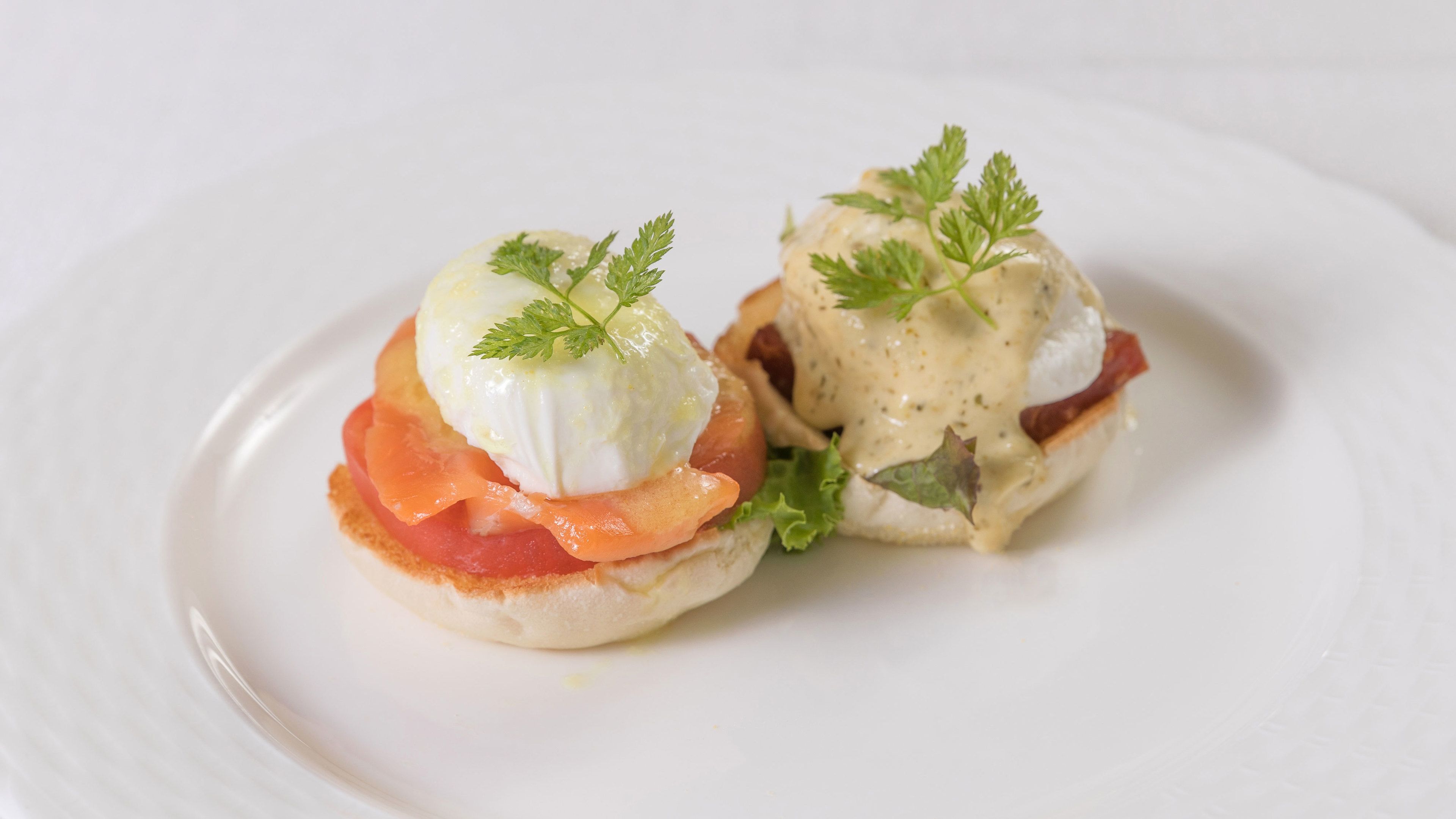 Dos sándwiches huevos benedictinos en un plato blanco.