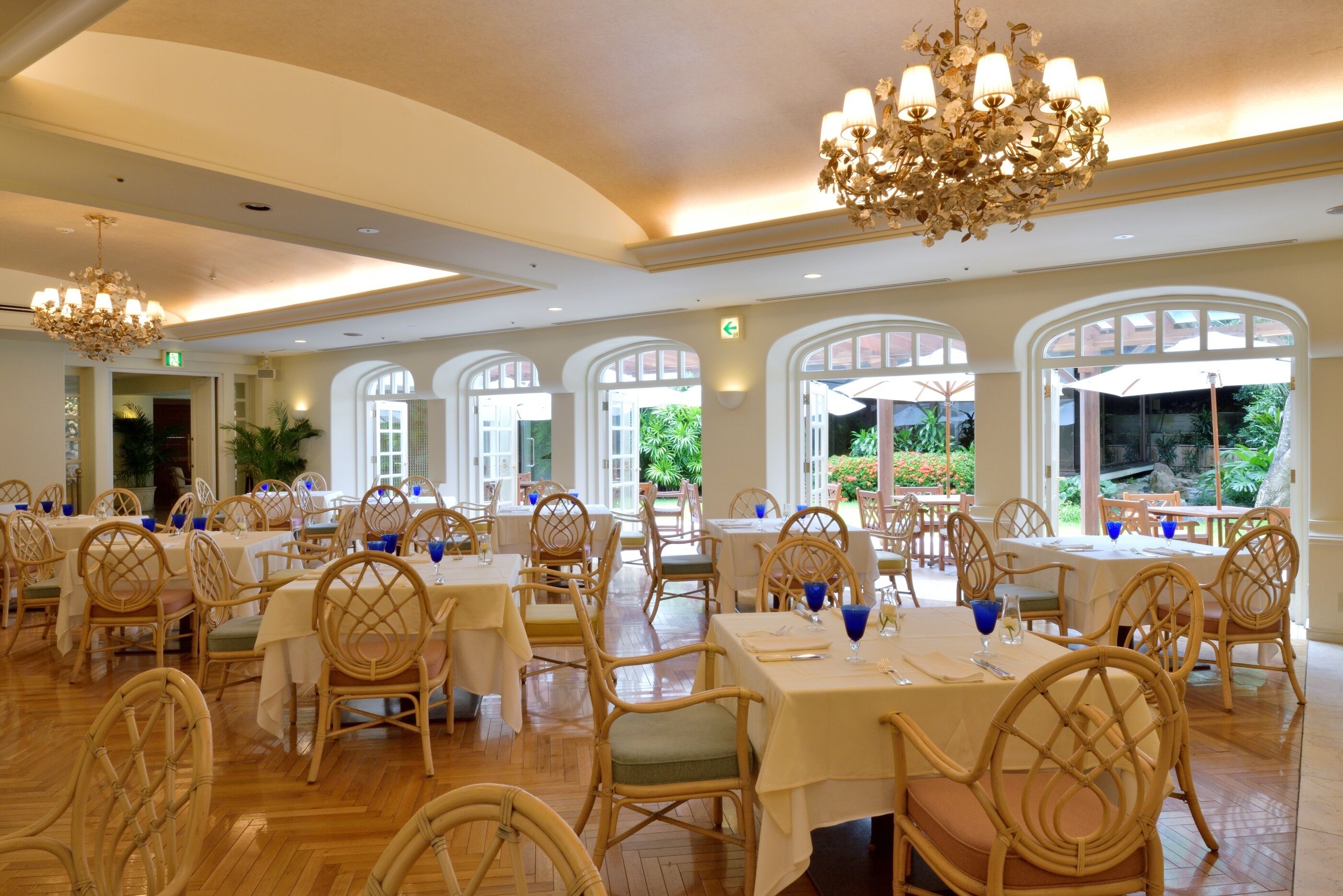A spacious dining area with high ceilings, chandeliers, and large windows offering views of the outdoors.