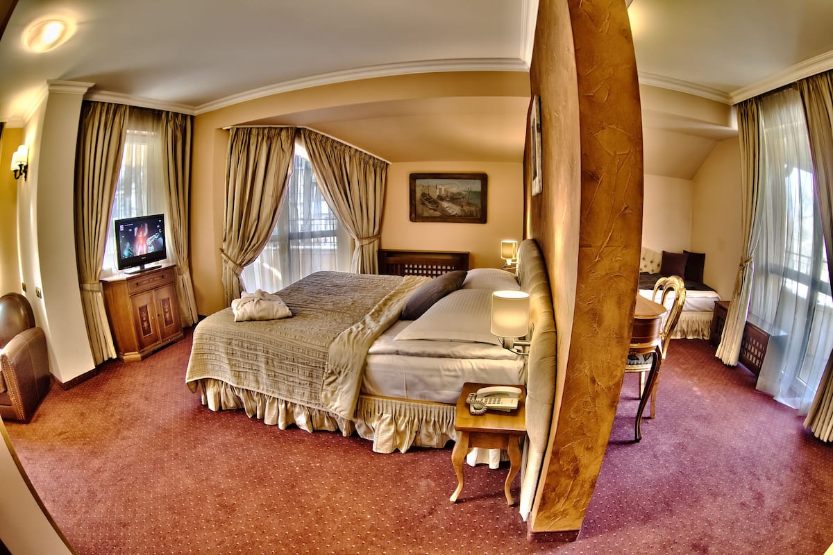 A spacious hotel room with a large bed, a television, a wooden nightstand, and a desk with a chair.