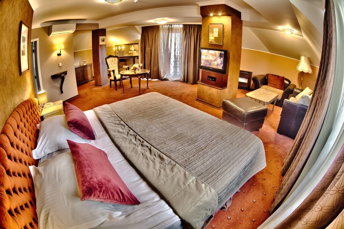 A hotel room with a large bed, a desk, a TV, and a dining area.