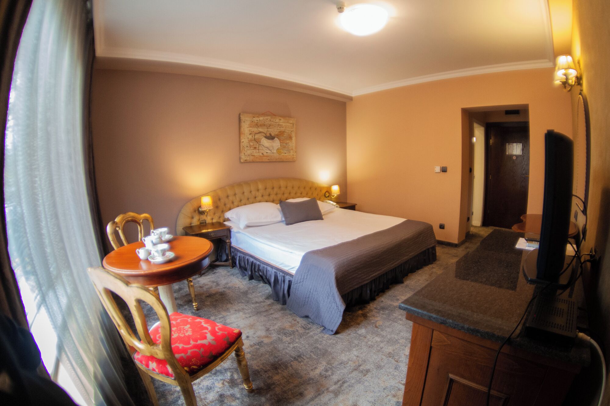 Quarto de hotel com cama, mesa de cabeceira, cadeira e escrivaninha com cadeira.