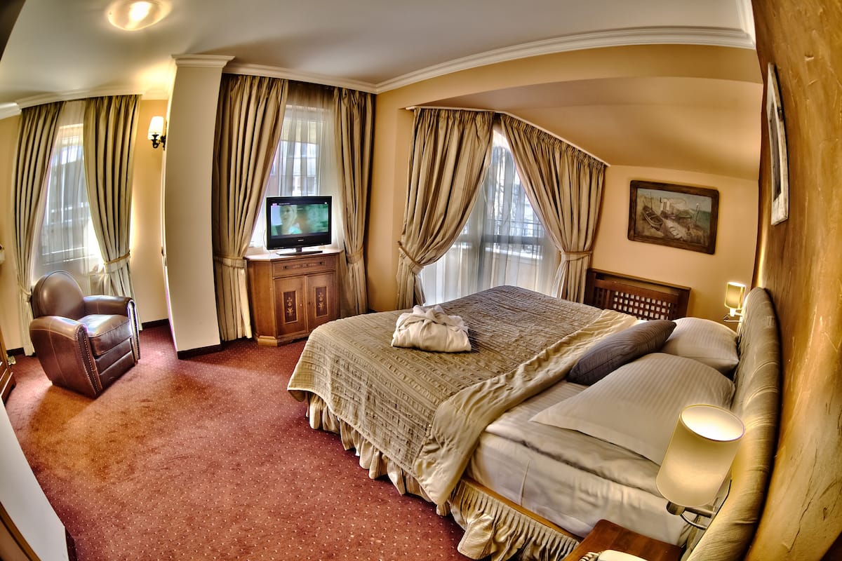 A hotel room with a large bed, a television, a chair, and a painting on the wall.