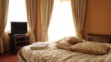 Una habitación de hotel con una cama, un televisor sobre un mueble y cortinas.