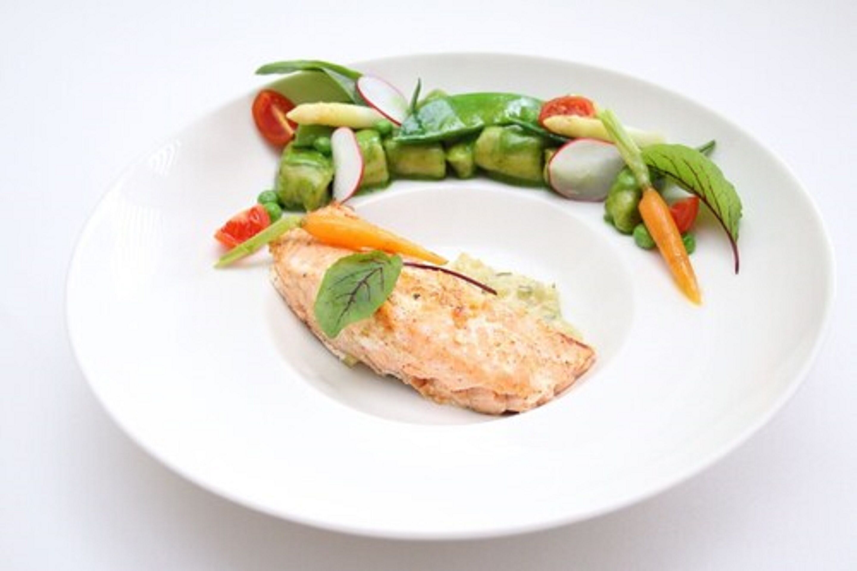 Une assiette comprenant un morceau de poisson grillé, une tranche d’avocat et une salade composée de différentes variétés de laitue, de radis et de tomates cerises.