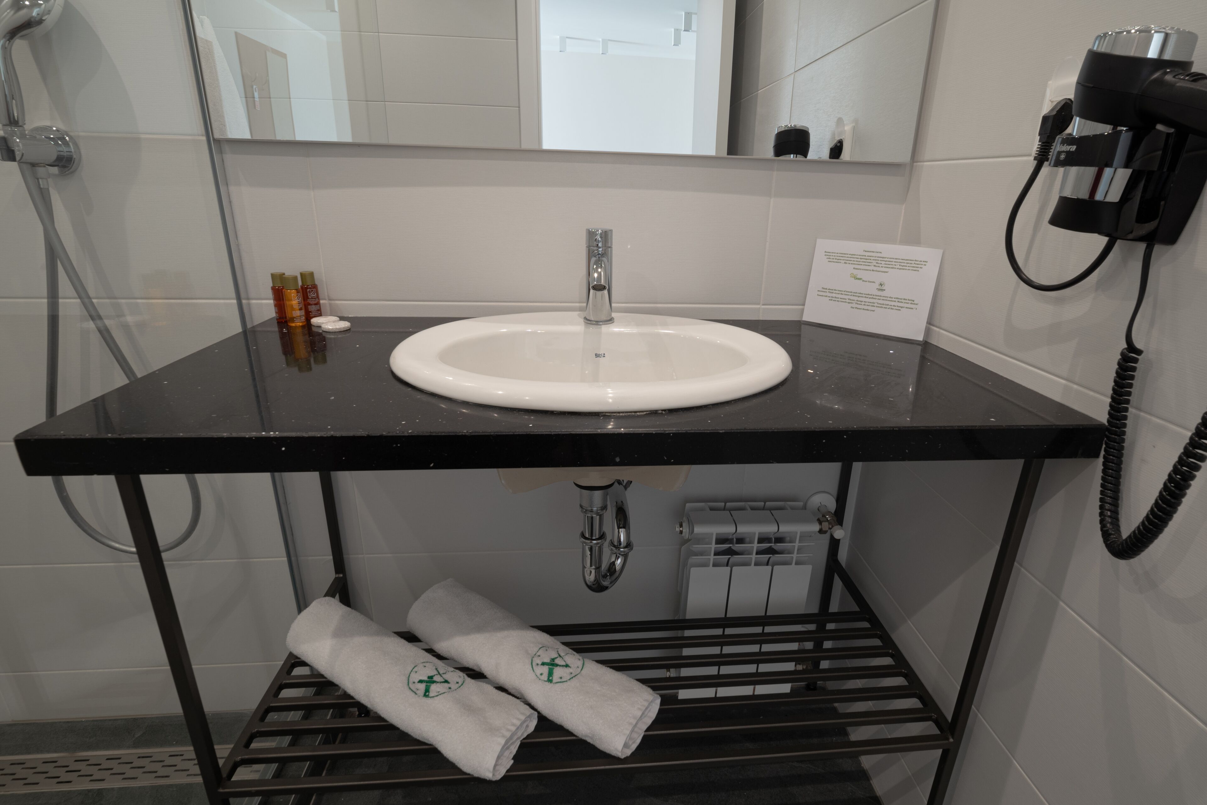 A modern bathroom with a black countertop, white sink, and a towel rack with towels.