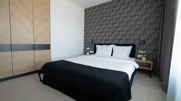 Una habitación de hotel moderna con una cama grande, un armario, un papel tapiz estampado y una mesita de noche con lámpara.