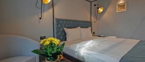 Una habitación de hotel moderna con una cama grande, una mesita con un jarrón de flores y dos luces fijadas a la pared.