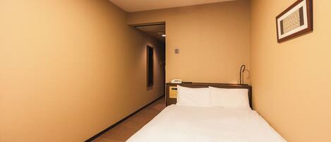 A hotel room with a single bed, a bedside table with a phone, and a framed picture on the wall.
