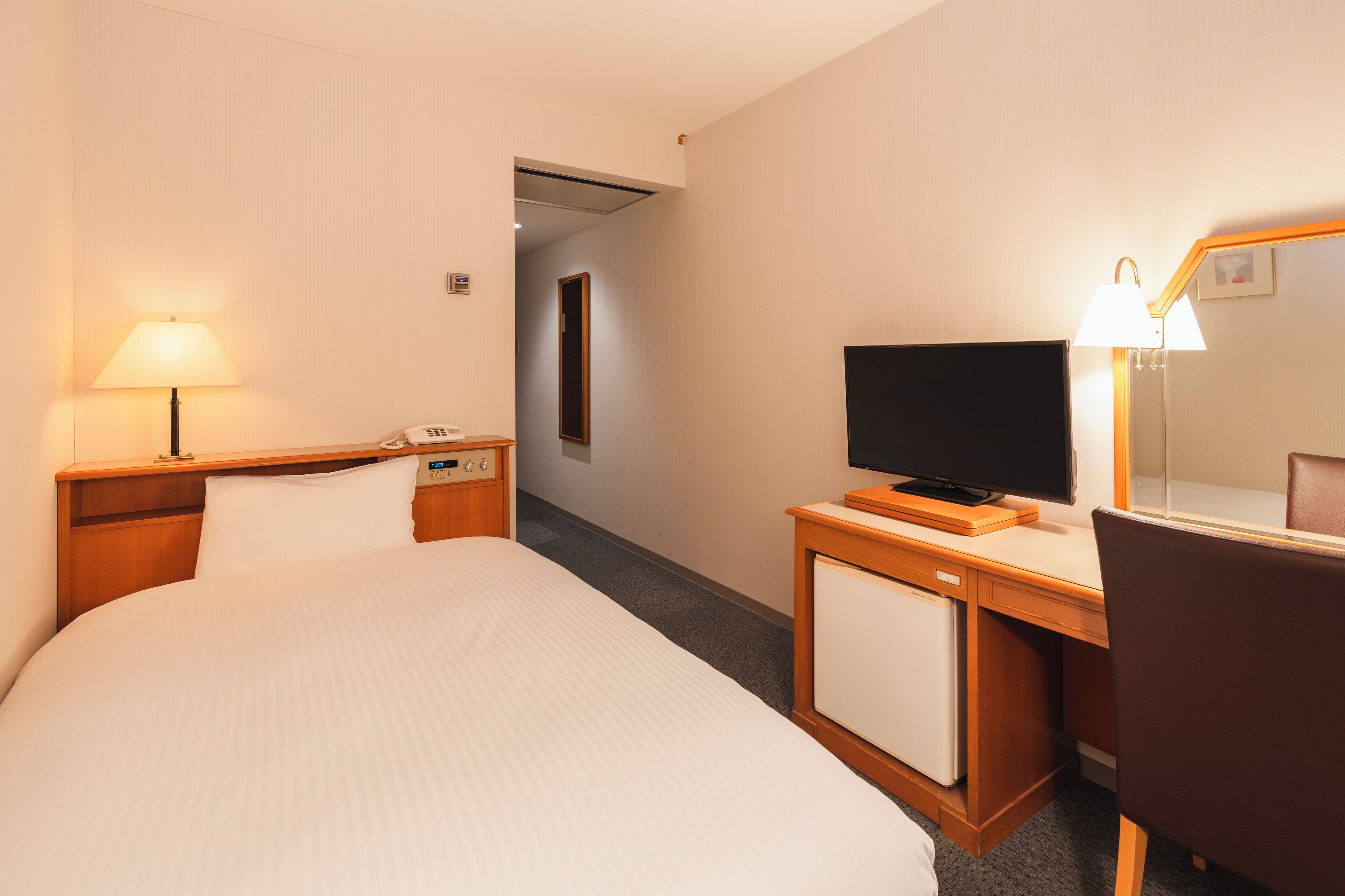 A hotel room with a bed, a desk with a computer, a TV, and a lamp.