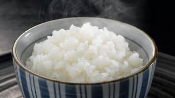 A bowl of white rice with steam rising from it, placed on a striped surface.