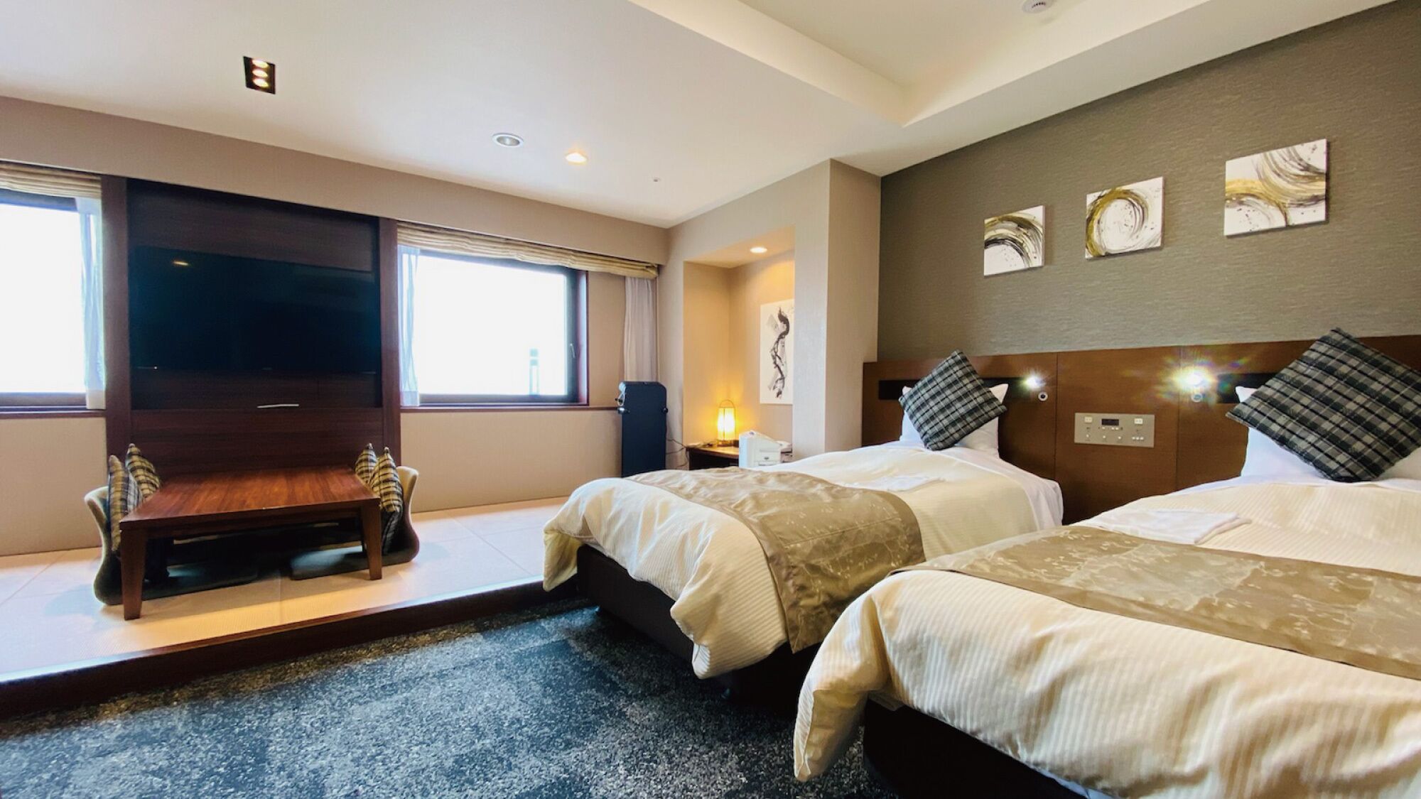 Ein Hotelzimmer mit zwei Betten, einem Flachbildfernseher, einem Schreibtisch und einem großen Fenster.