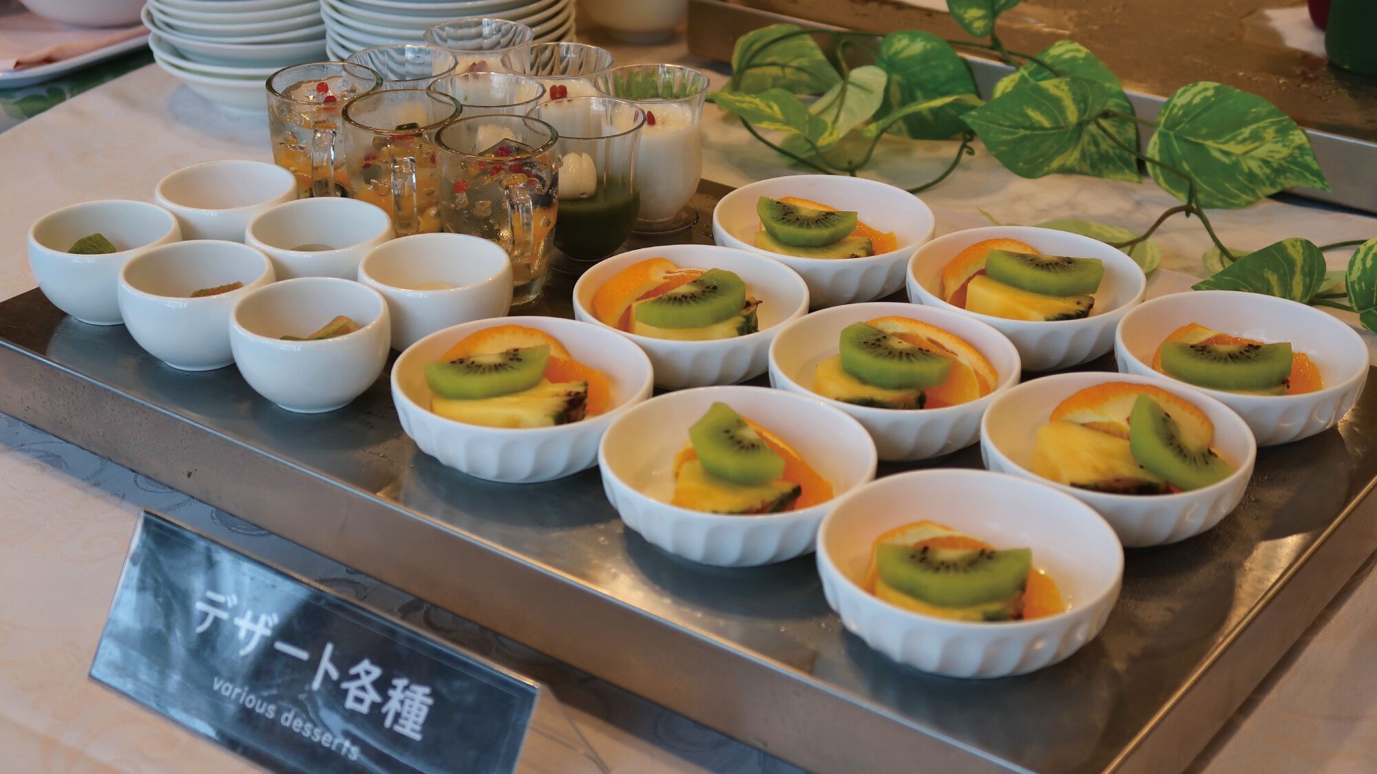 Exposição de sobremesas com diversos doces cobertos de fruta em tigelas brancas.