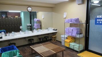 A public restroom with a long counter, multiple sinks, a clock, and shelves with folded towels.