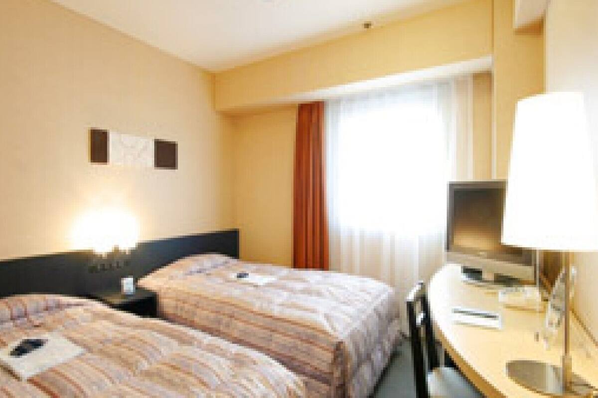 Une chambre d’hôtel avec deux lits, un bureau avec une chaise, une télévision et une fenêtre avec des rideaux.