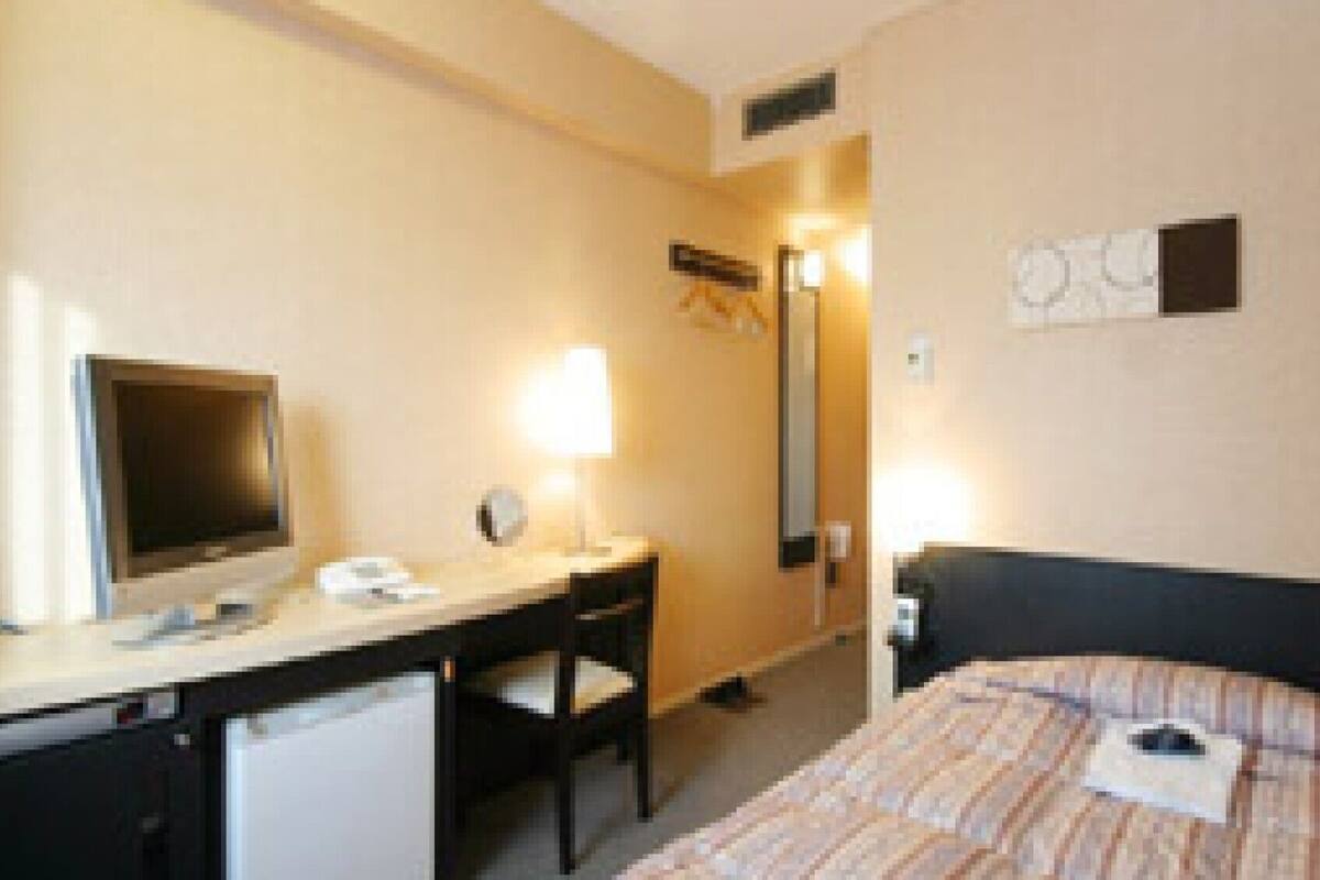 Une chambre d’hôtel équipée d’un lit, d’un bureau, d’une chaise, d’une télévision et d’un miroir.