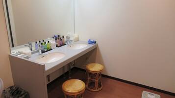 A bathroom with two sinks, a mirror, toiletries, and two wicker stools.