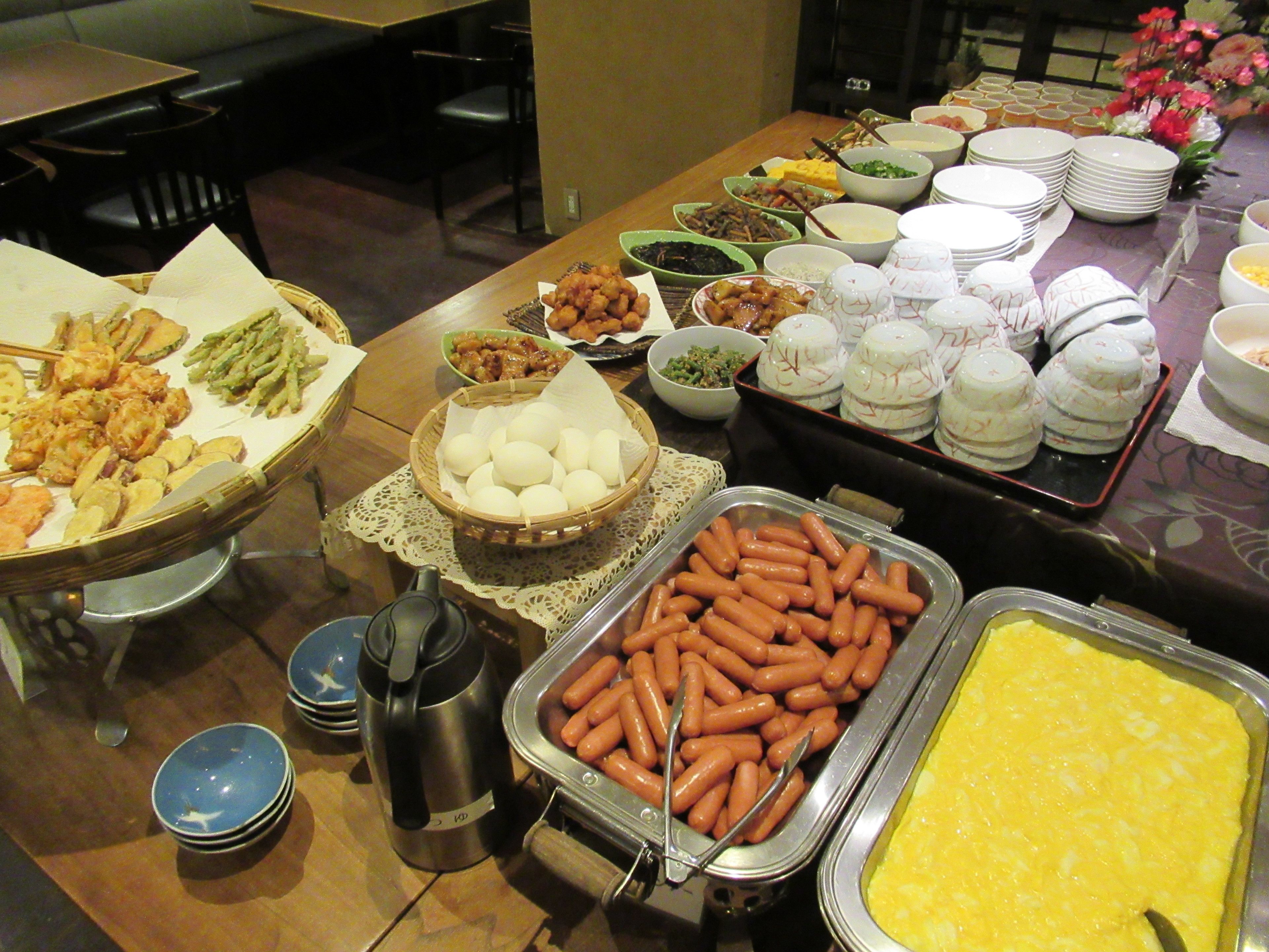 A buffet table with various dishes including hot dogs, eggs, and other food items.
