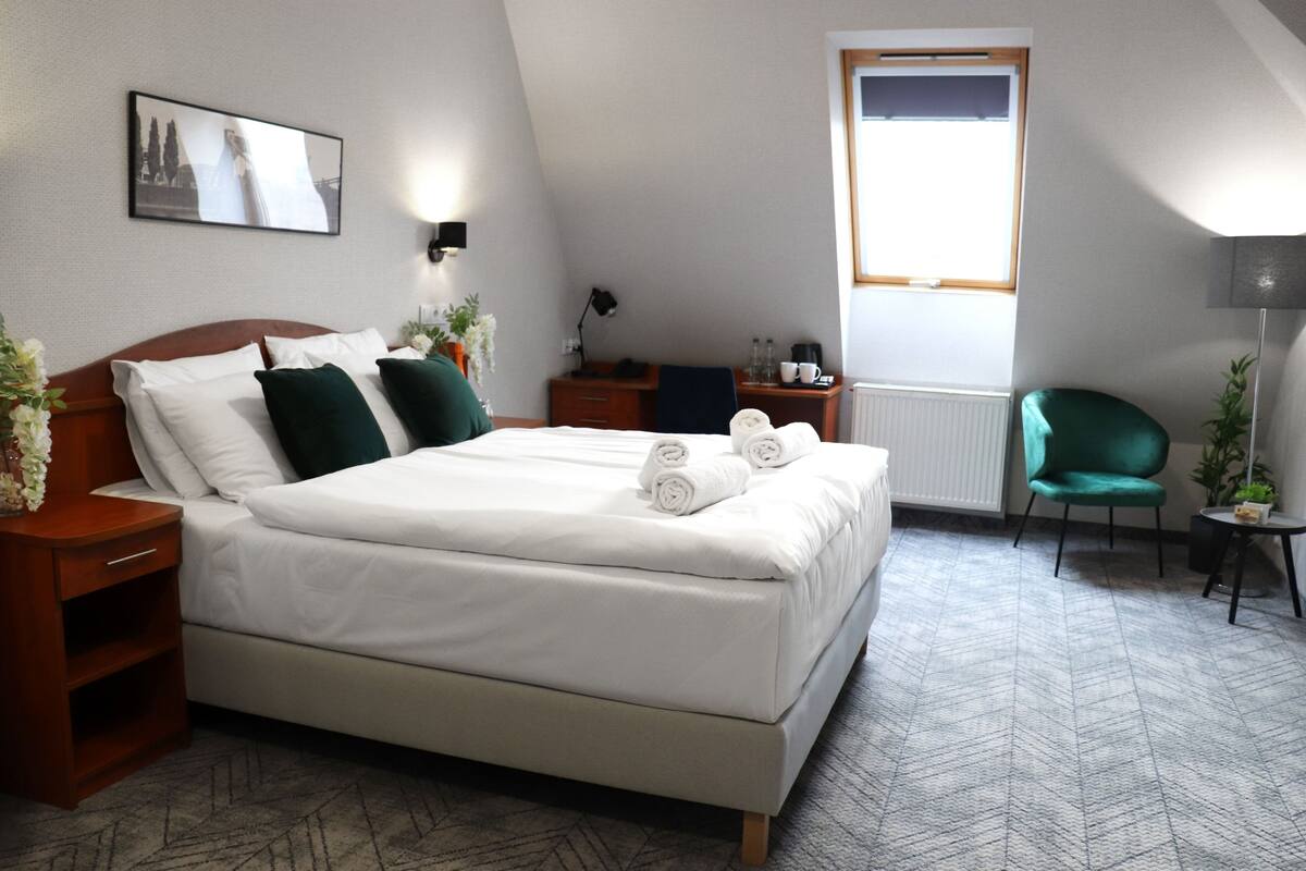 A neatly arranged bedroom with a large bed, a desk, a chair, and a window.