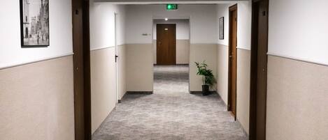 Un pasillo de hotel con alfombra estampada, puertas de madera y una señal de salida verde.