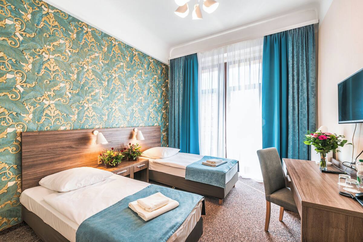 A hotel room with two beds, a desk, and a TV.