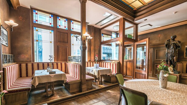 A restaurant with wooden booths, tables, and a statue. - Hotel Polonia (Wroclaw)