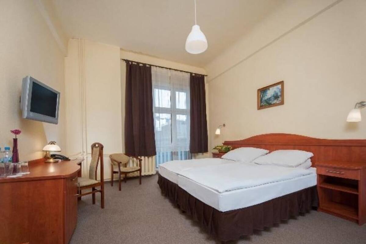 A hotel room with a bed, desk, chair, television, and a window with curtains.