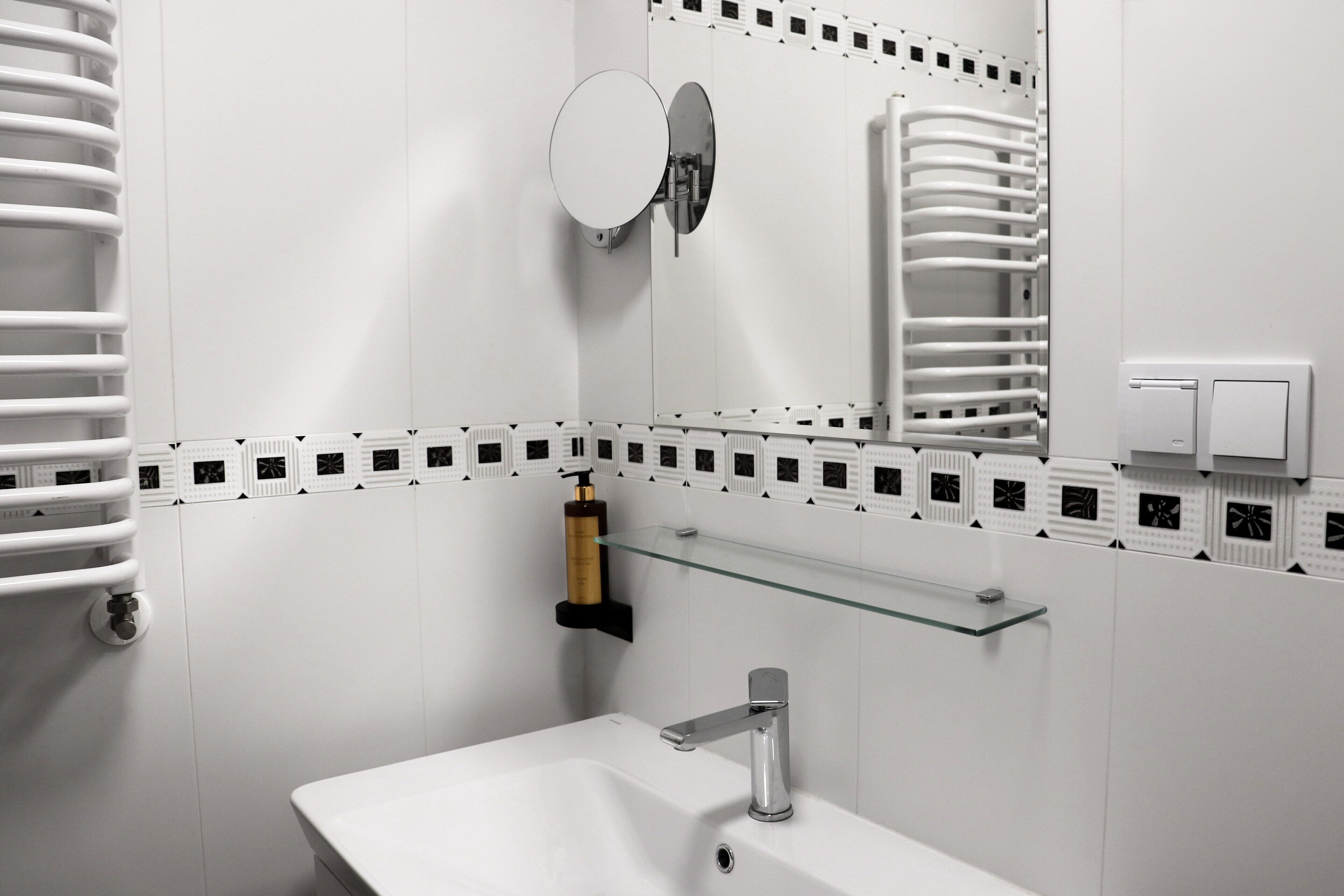 Une salle de bain moderne avec un lavabo blanc, un miroir et une étagère en verre.