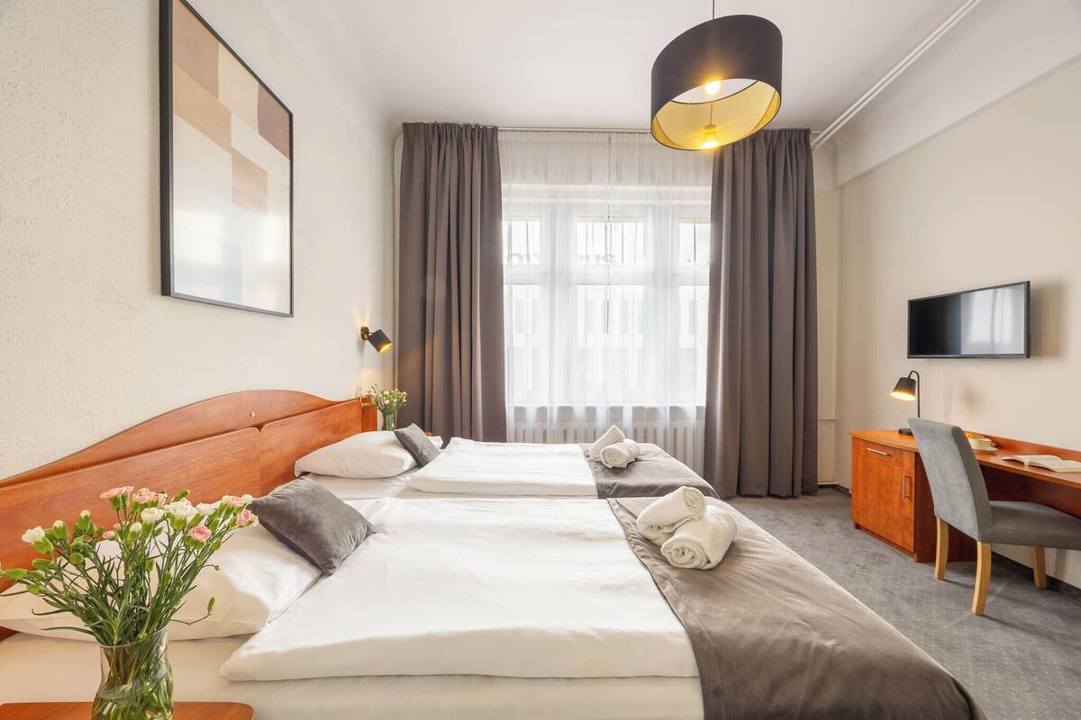 A hotel room with a large bed, a desk, a chair, a TV, and a window with curtains.