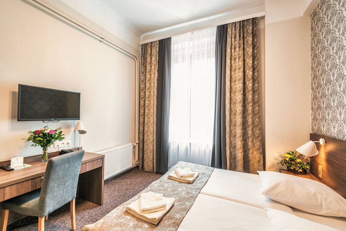 A hotel room with a bed, a desk, a chair, a TV, and a window with curtains.