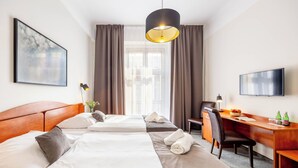 A hotel room with two beds, a desk, a chair, a TV, and a large window with curtains. - Hotel Polonia (Wroclaw)